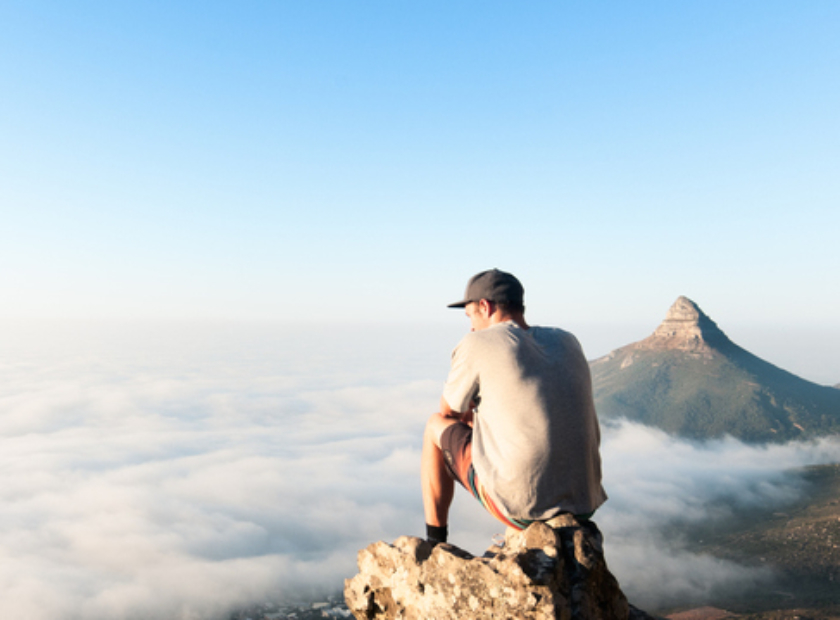Young man sitting on mountain above the clouds