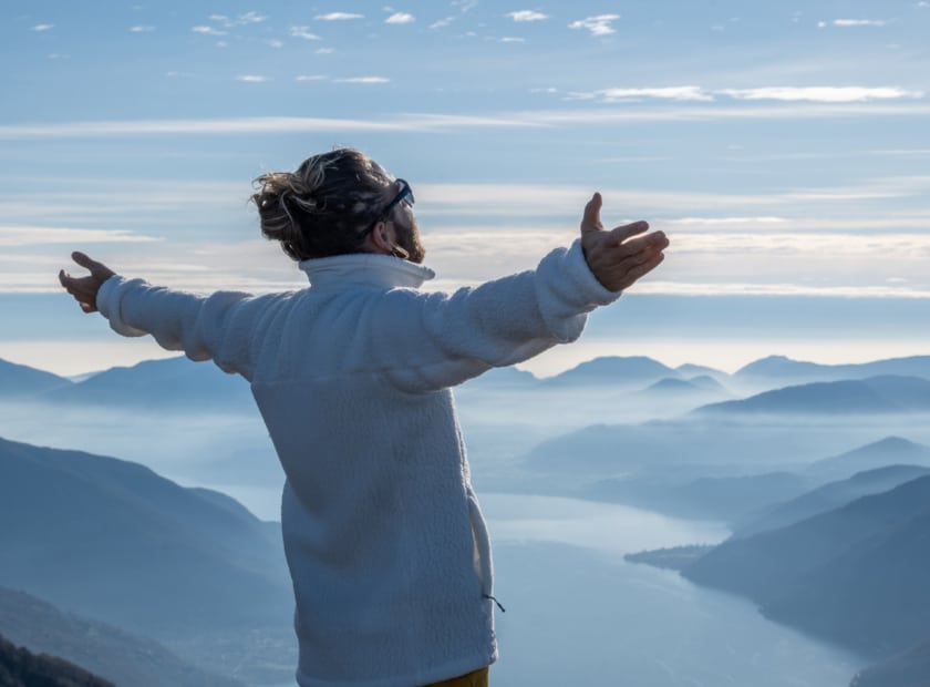 Hiker stands arms out on mountain top