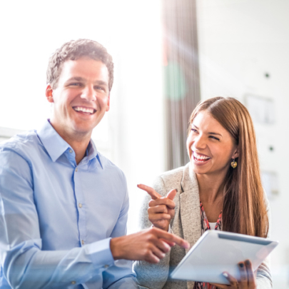 Portrait of cheerful businessman with female colleague using digital tablet in office
