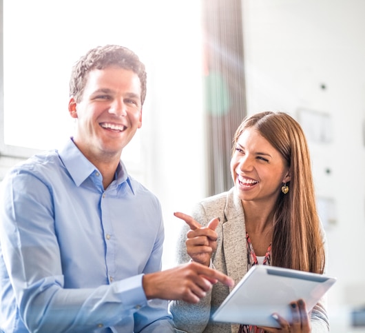 Portrait of cheerful businessman with female colleague using digital tablet in office