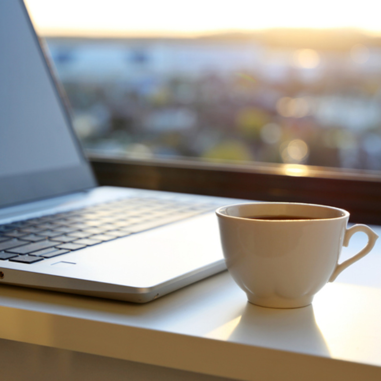 Kahvikuppi ja kannettava tietokone pöydällä auringon noustessa