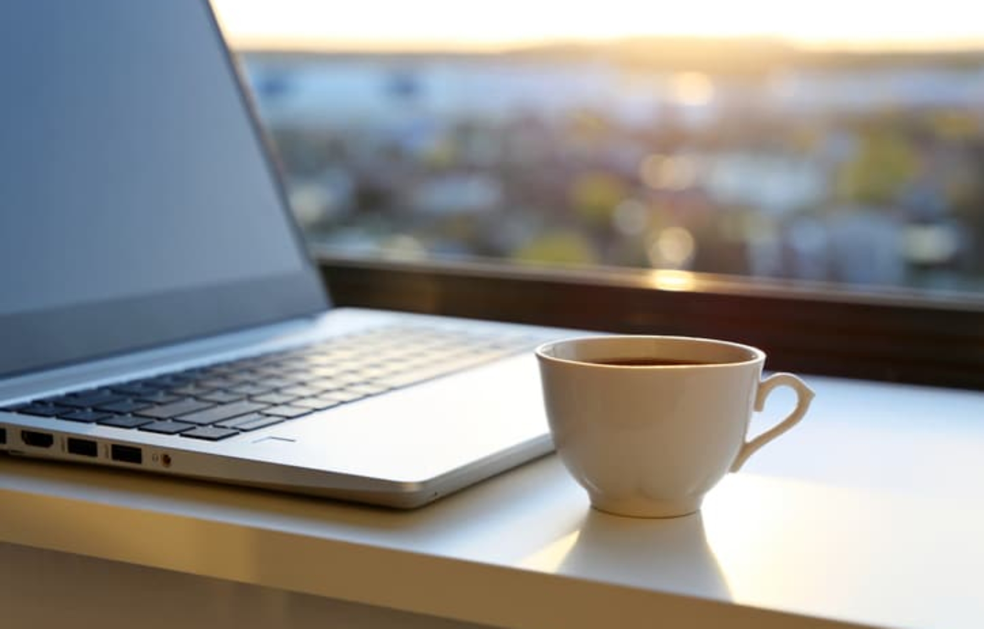 Coffe cup and laptop on desk at sunrise
