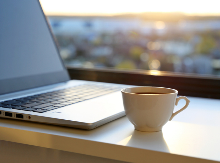 Kaffekopp och bärbar dator på skrivbordet vid soluppgången